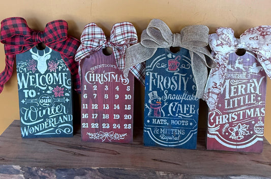 Set of Christmas-themed wooden tags with decorative bows on a wooden surface.