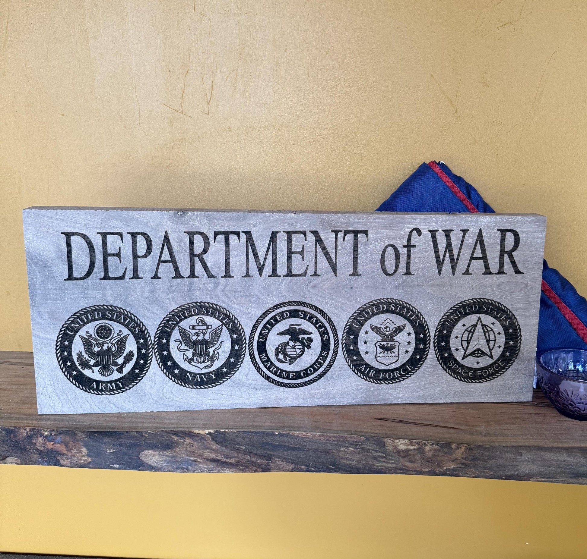 Wooden sign with 'DEPARTMENT of WAR' and military emblems on a wooden surface.