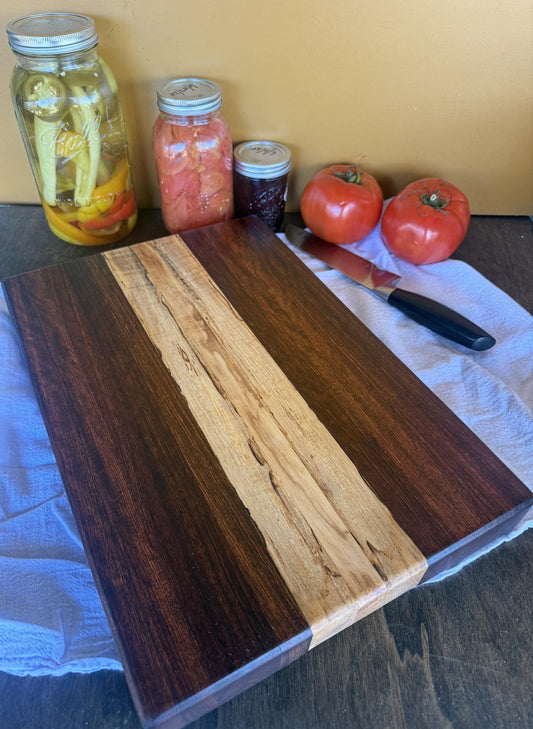 Wooden cutting board with jars of pickled vegetables, tomatoes, and a knife on a table.