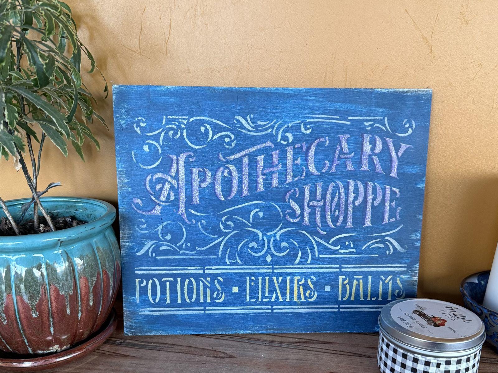 Blue sign with 'Apothecary Shoppe' text next to a potted plant and a jar.