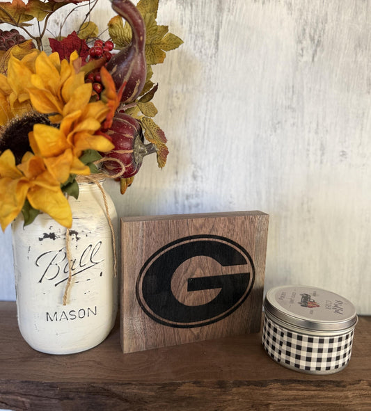 Decorative items including a mason jar with flowers, a wooden block with Georgia University logo, and a small tin can on a wooden surface.