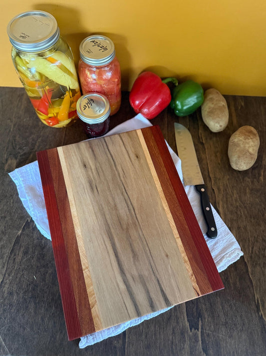 Wooden cutting board with jars of pickled vegetables and a knife on a wooden surface.