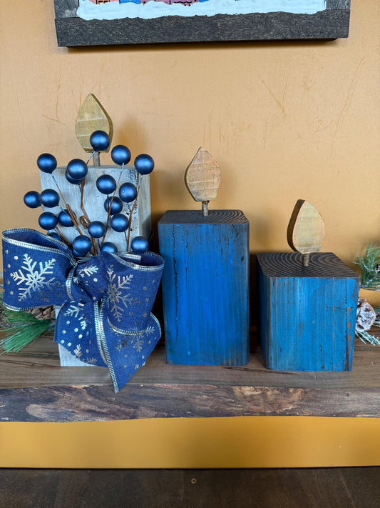 Wooden blue candles with a bow with snowflake design on a wooden surface.
