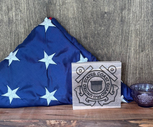 Wooden plaque with U.S. Coast Guard emblem next to a folded American flag on a wooden surface.