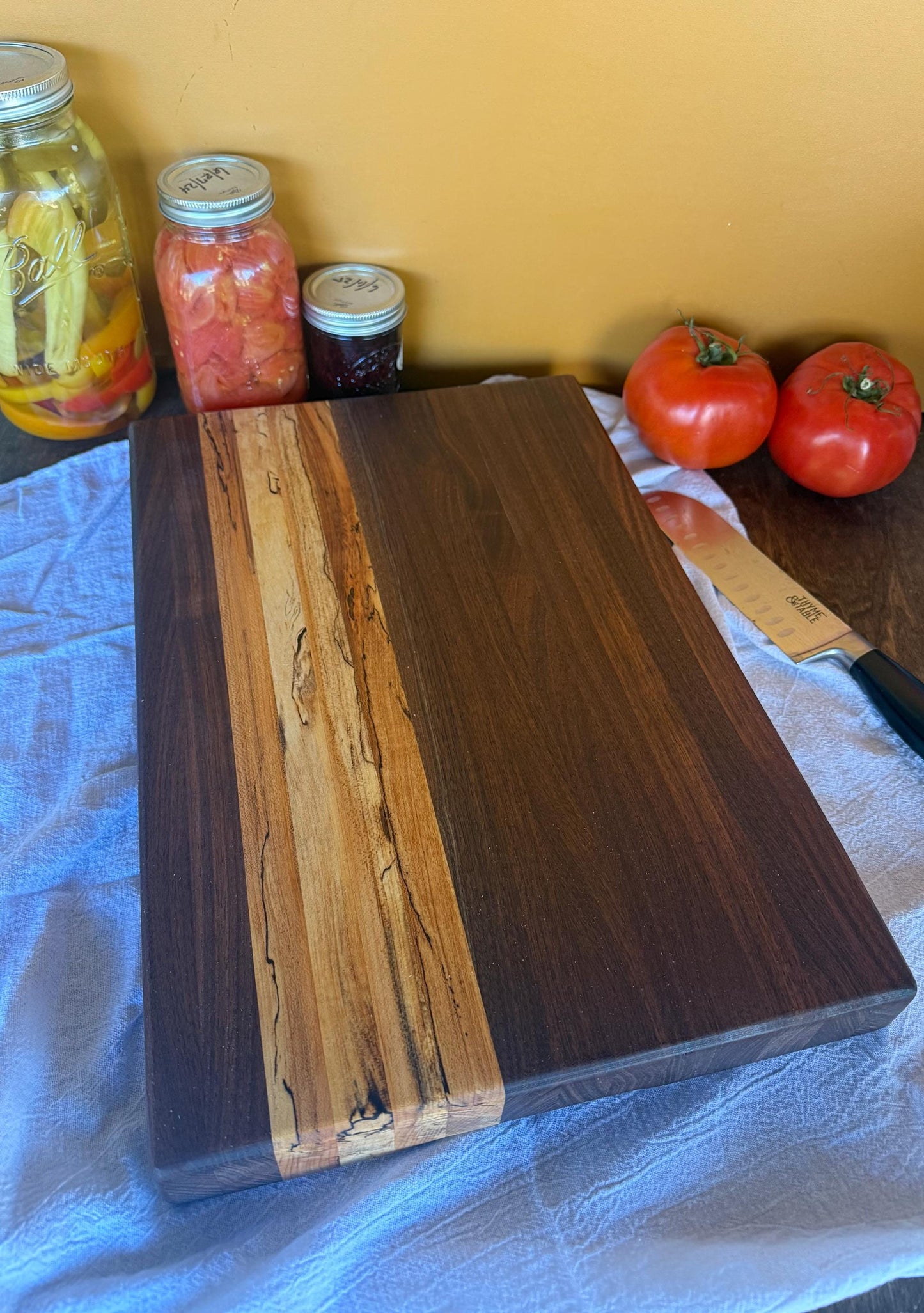 Wooden cutting board with tomatoes and jars on a table