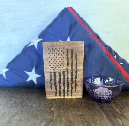 Wooden block with American flag design in front of a blue flag on a wooden surface