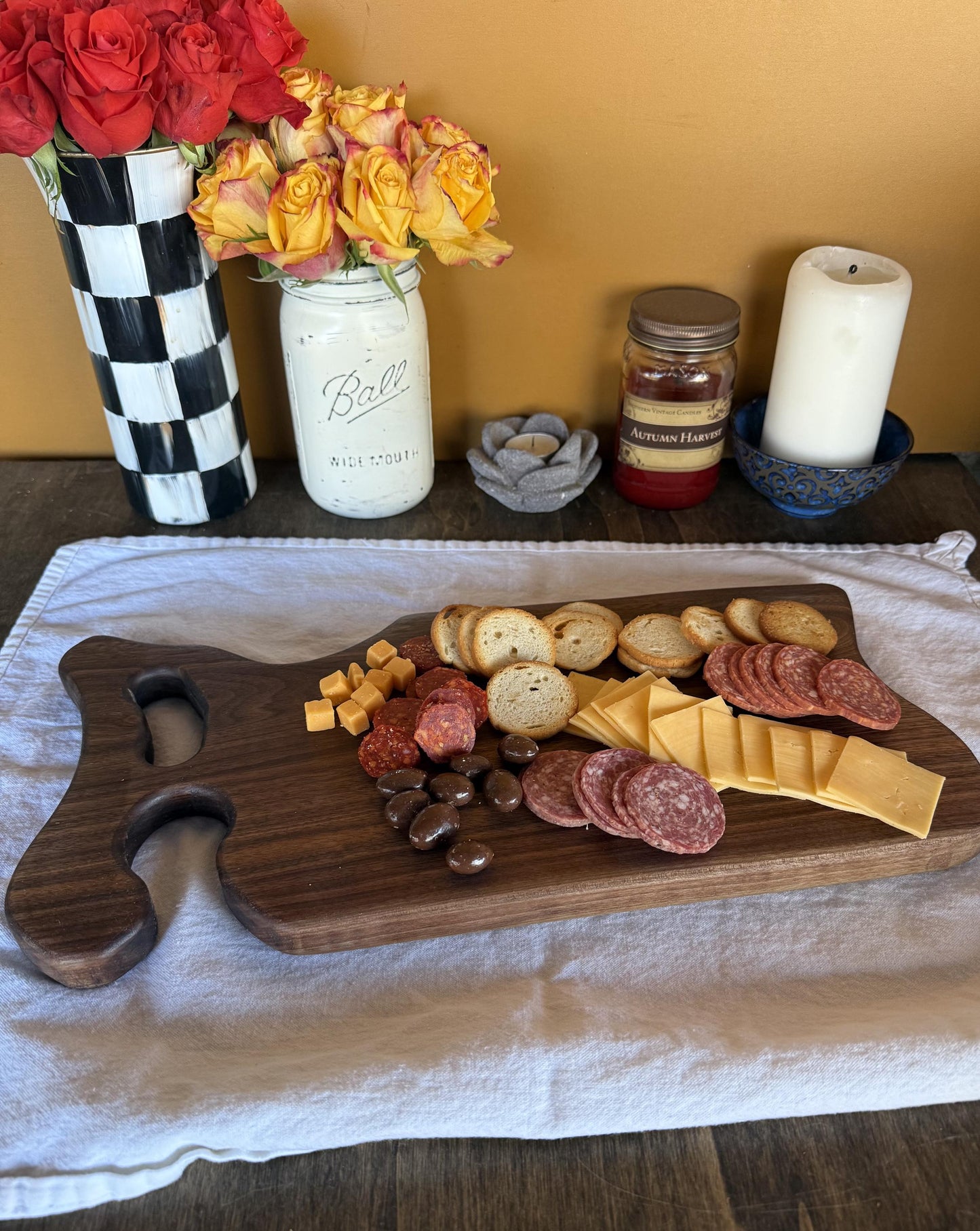 Wooden charcuterie board with meats, cheeses, and bread on a table with decorative items.