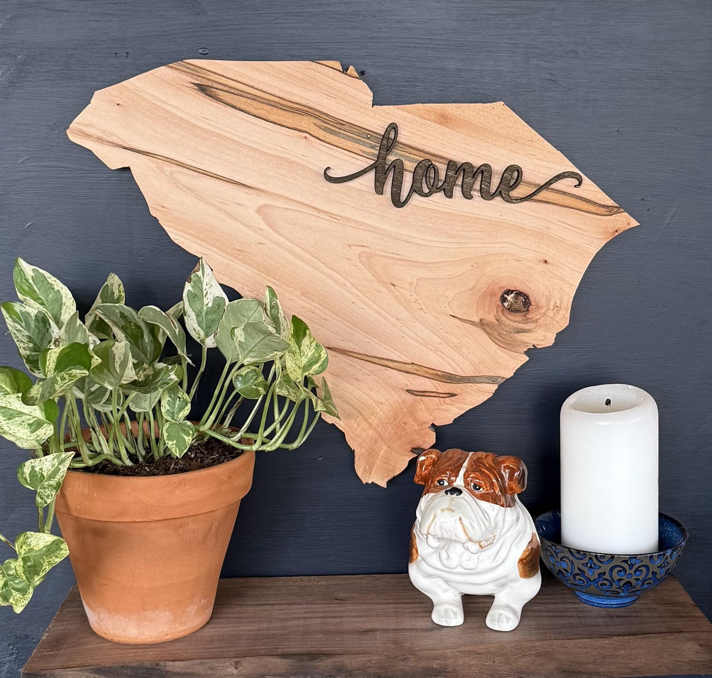 Wood South Carolina with 'home' wood cutout, potted plant, ceramic dog figurine, and candle on a dark surface.