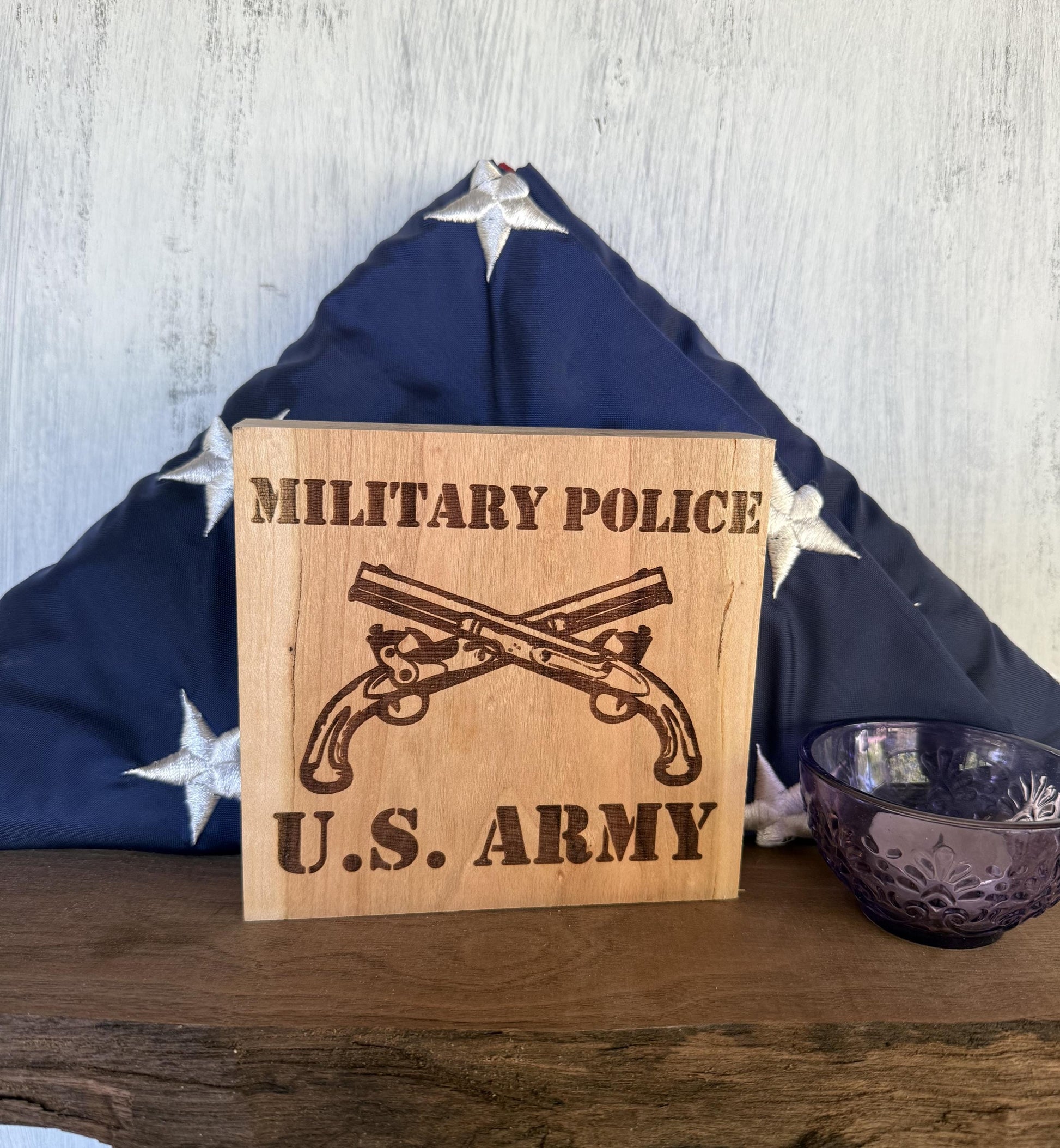 Wooden sign with 'Military Police U.S. Army' engraving in front of a folded American flag.