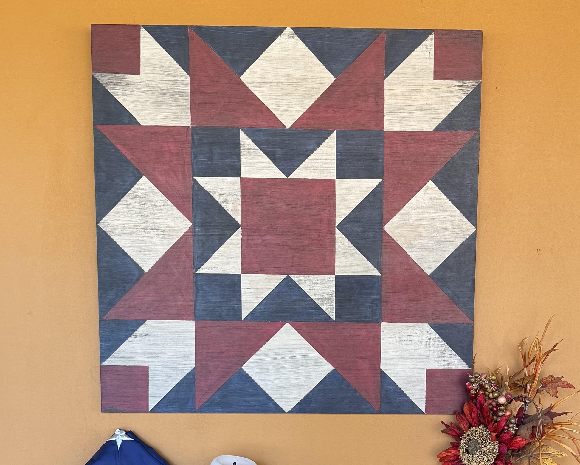 Red, white and blue barn quilt with geometric star pattern on a yellow wall