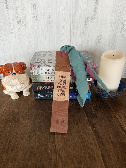Stack of books with a wooden bookmark that says "Pet Dogs, Read Books, Be Happy" and a candle on a wooden surface.
