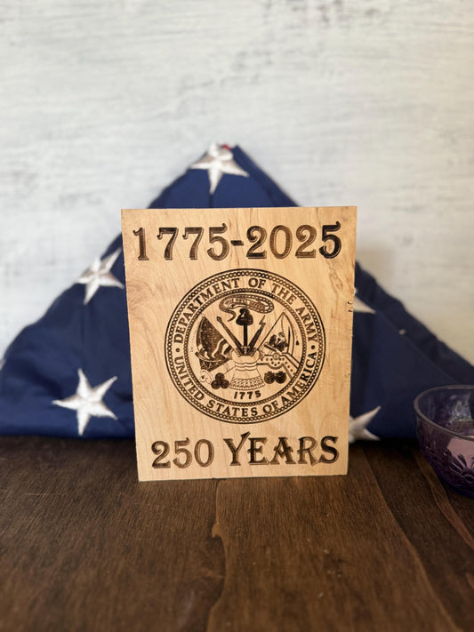 Wooden plaque with '1775-2025 250 Years' text and U.S. Army emblem on a wooden surface.