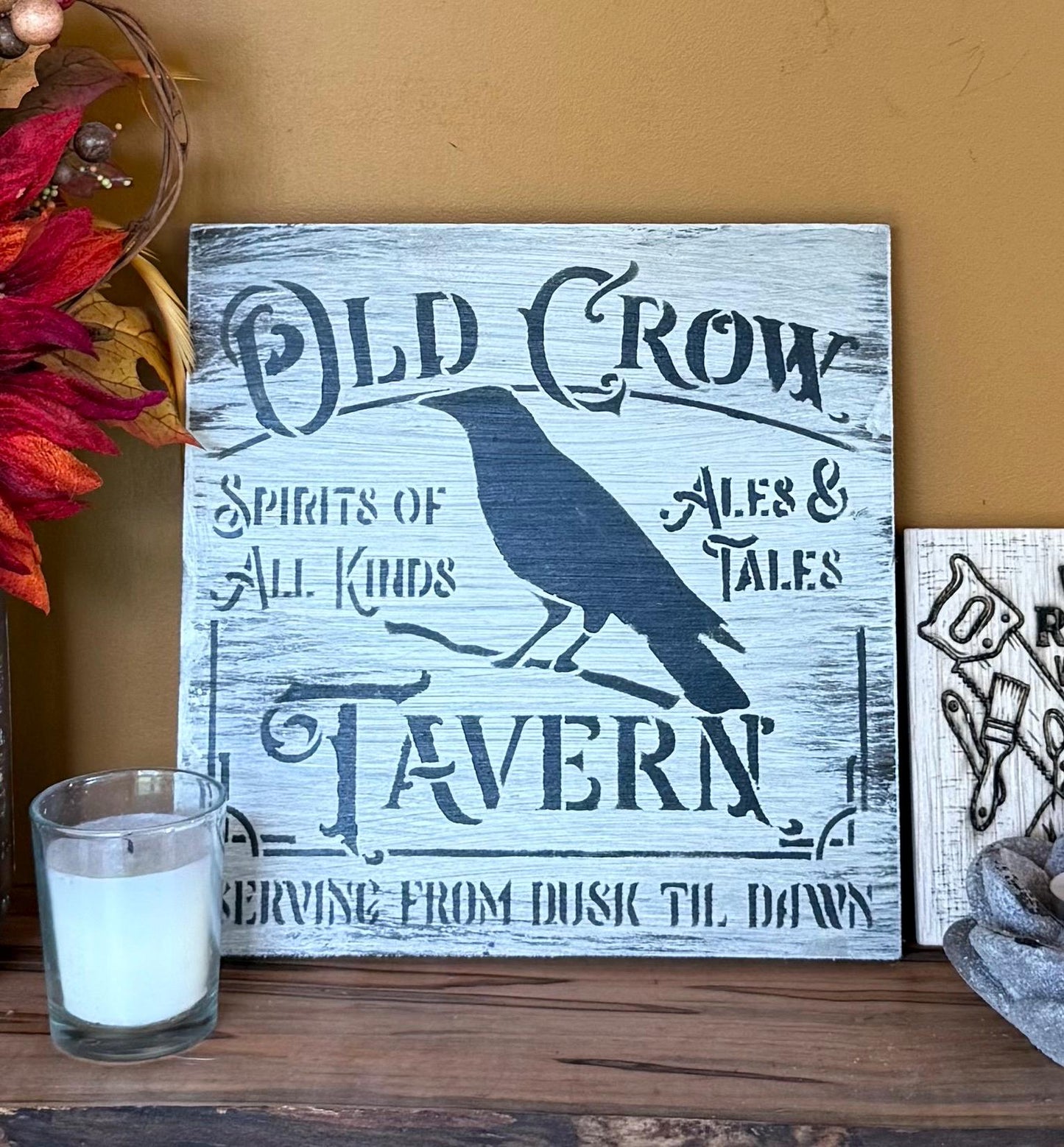 Wooden sign with 'Old Crow Tavern' design on a wooden surface with a candle and decorative elements.