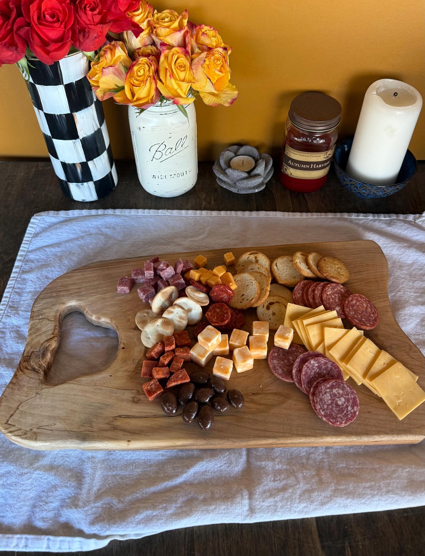 Wooden charcuterie board with assorted meats, cheeses, and dried fruits on a table with decorative items.