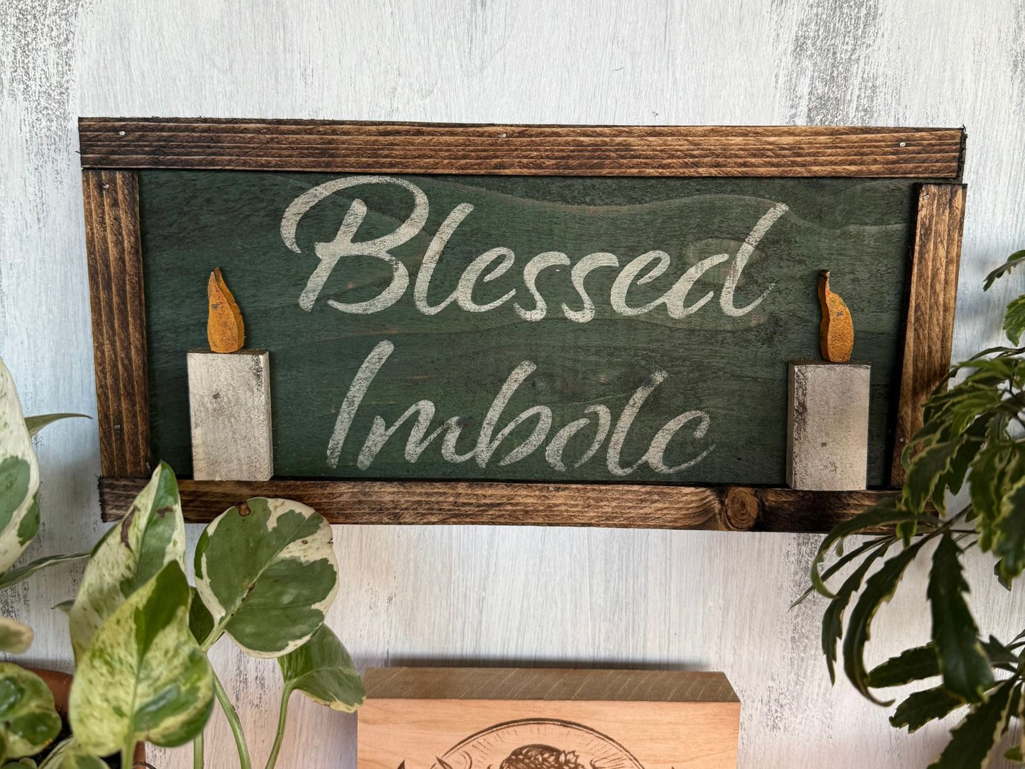 Decorative sign with 'Blessed Imbolc' text and candles on a wooden frame, against a light background.