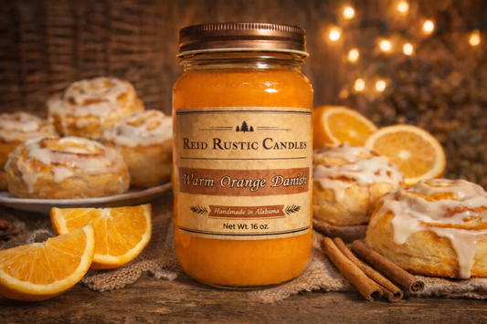 Jar of Reid Rustic Candles Warm Orange Danish candle with orange rolls and oranges on a wooden surface.