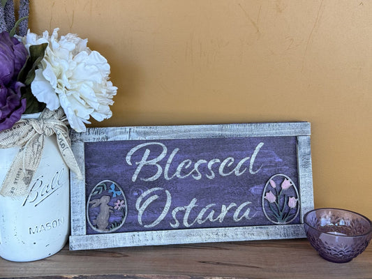 Decorative sign with 'Blessed Ostara' text, flowers, and a mason jar on a wooden surface.