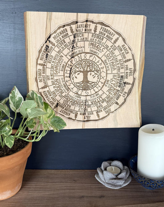 Wooden wall art with engraved Wheel of the Year Design on a dark blue wall with decorative items.