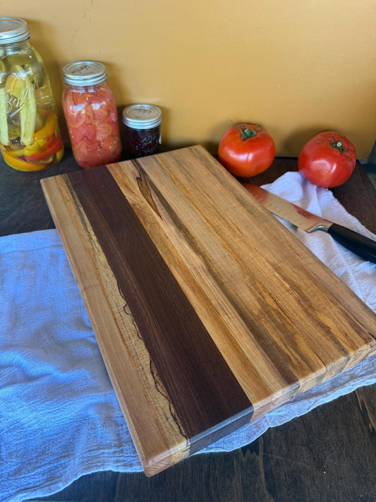 Wooden cutting board on a table with tomatoes and jars in the background