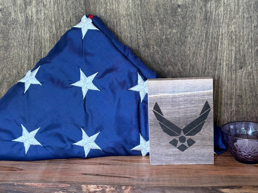 American flag folded neatly with a wooden plaque featuring an Air Force emblem on a wooden surface.