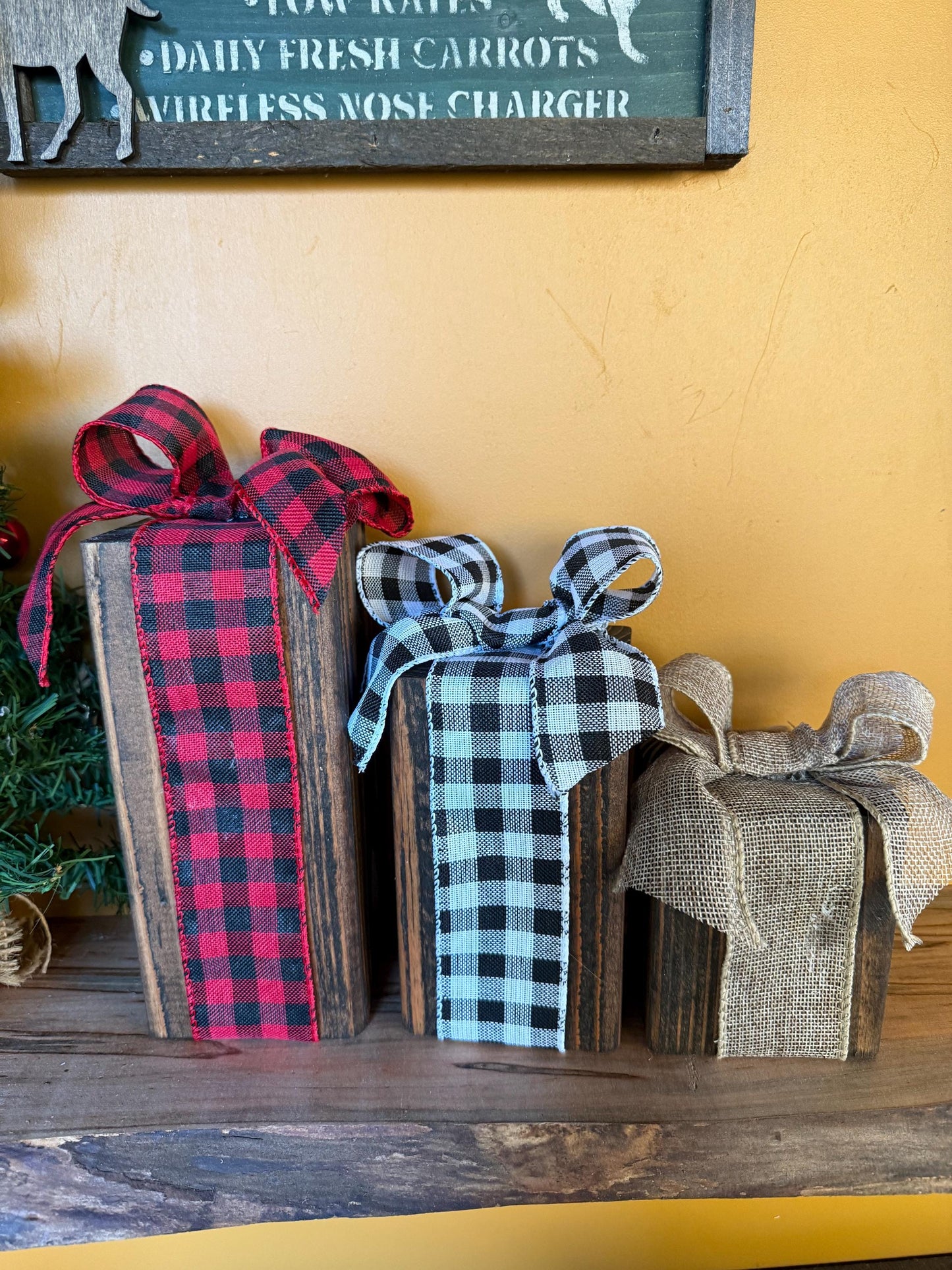 Wooden gift boxes with plaid ribbons on a wooden surface against a yellow wall.