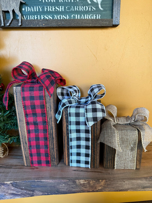 Wooden gift boxes with plaid ribbons on a wooden surface against a yellow wall.