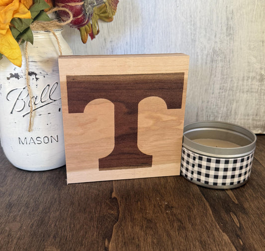 Wooden block with University of Tennessee logo next to a mason jar and checkered container on a wooden surface.