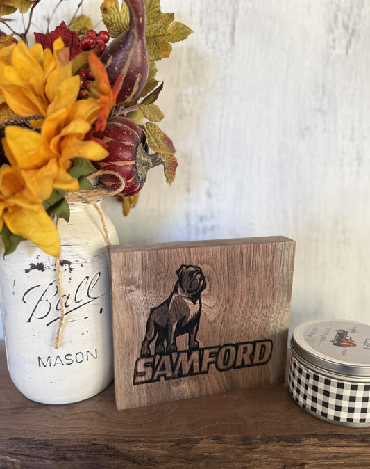 Decorative setup with a mason jar, wooden block with 'Samford' and dog illustration, and checkered container on a wooden surface.