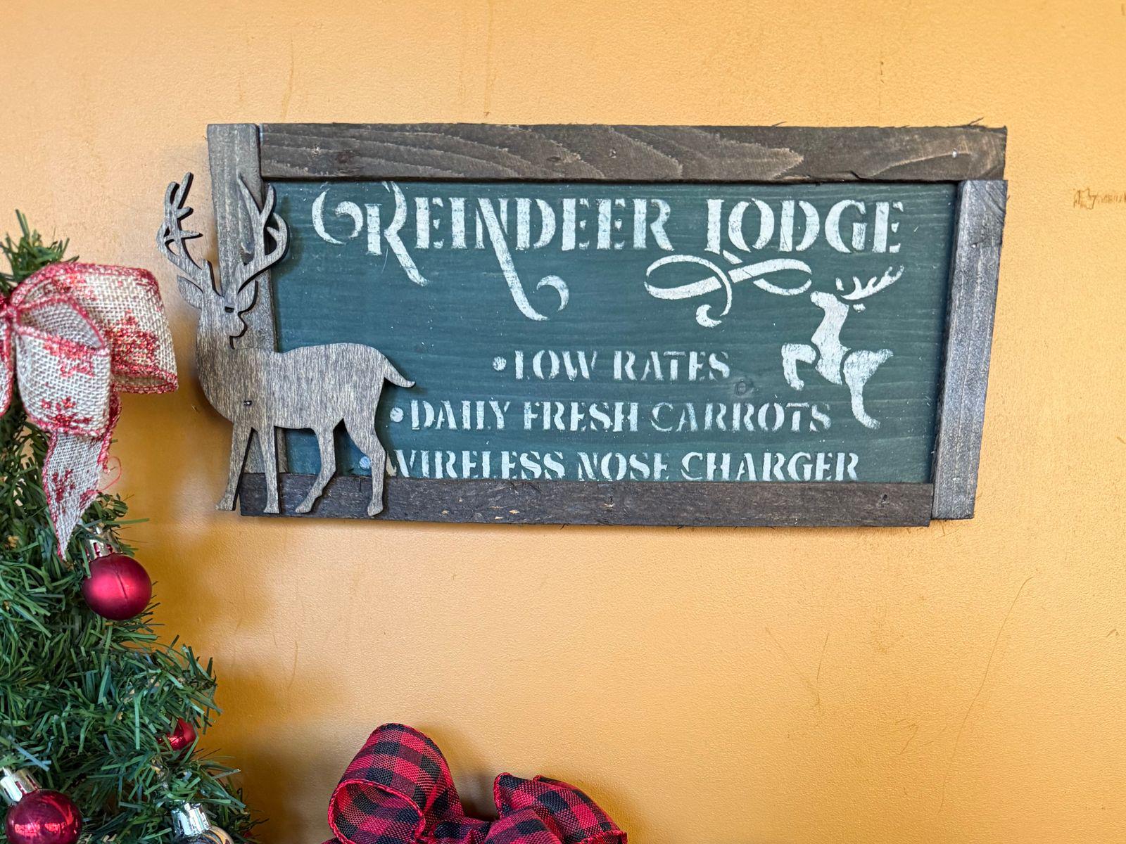 Wooden sign with reindeer design and text on a yellow wall.