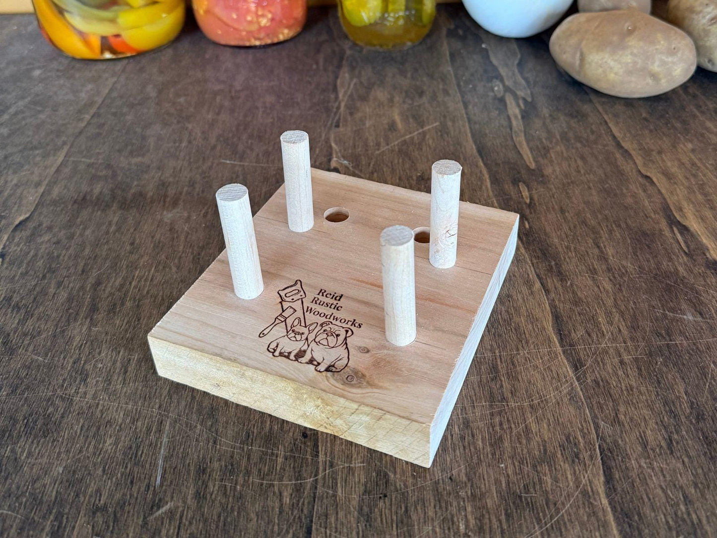 Wooden adjustable cutting board holder on a wooden surface with jars and vegetables in the background.