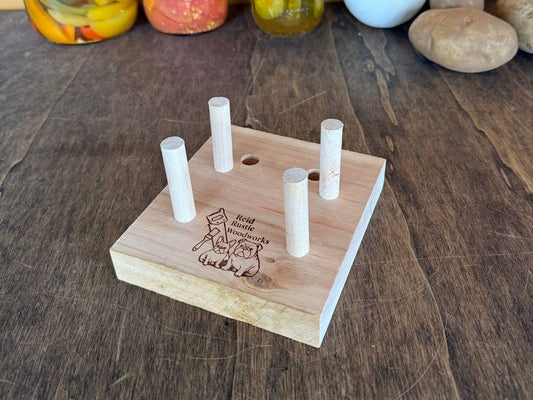 Wooden adjustable cutting board holder on a wooden surface with jars and vegetables in the background.