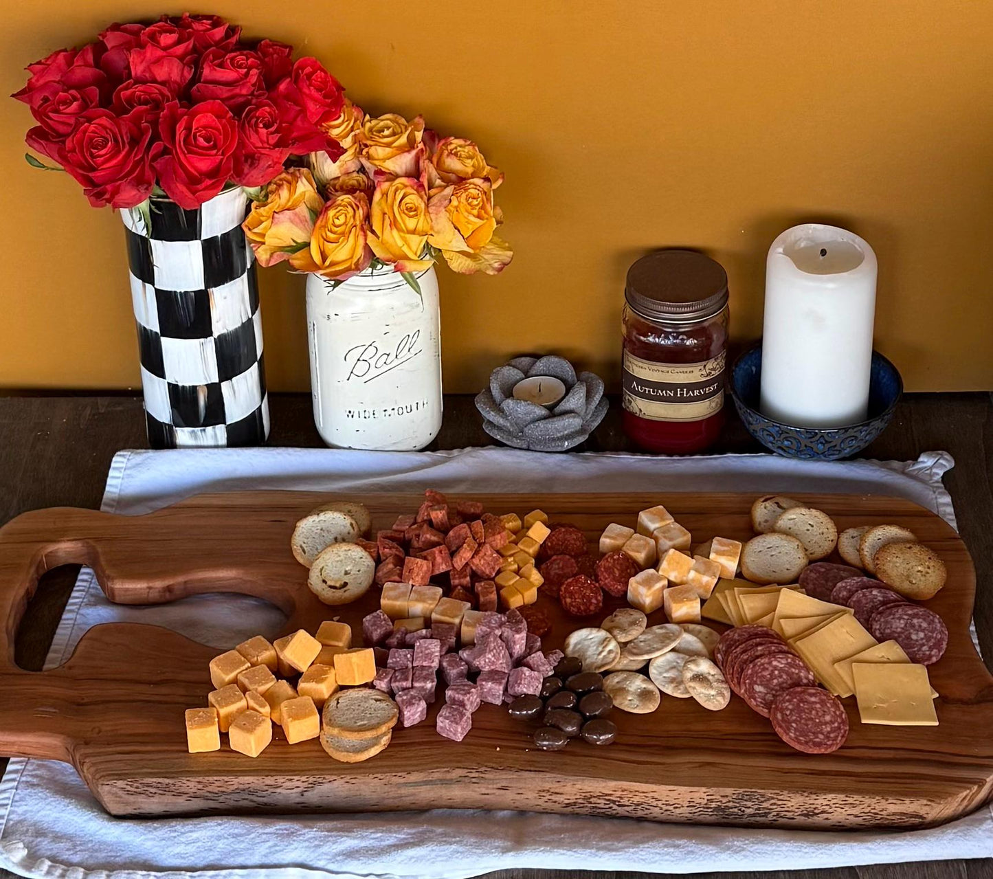 Wooden charcuterie board with various meats, cheeses, and crackers on a yellow wall background.