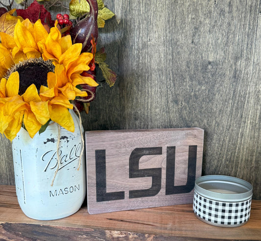 Decorative setup with sunflowers in a mason jar, 'LSU' sign, and small candle on a wooden surface.