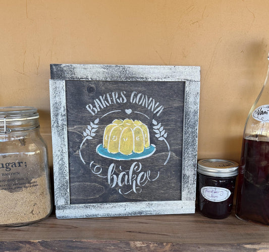 Wooden sign with a yellow cake illustration and text that says "Bakers Gonna Bake" on a shelf with jars and bottles.
