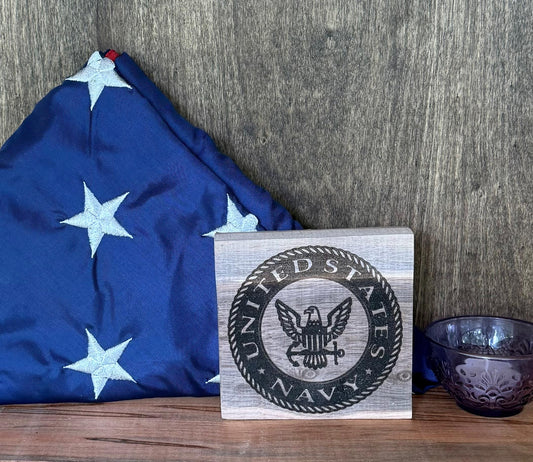 United States Navy emblem on a wooden plaque with a folded flag in the background.