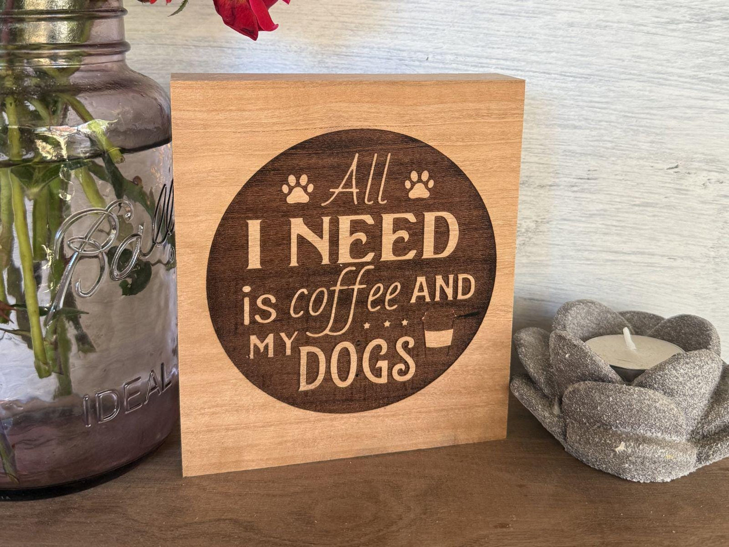 Wooden sign with 'All I need is coffee and my dogs' text on a wooden shelf.