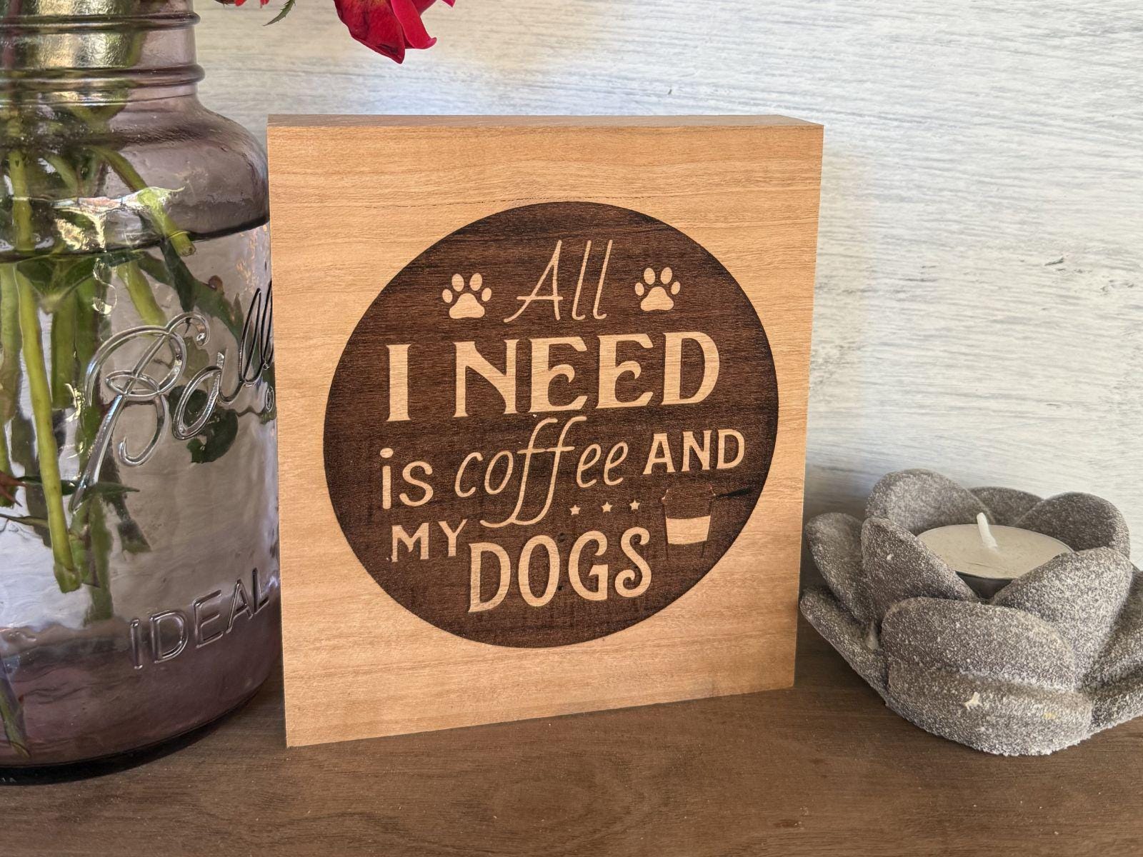 Wooden sign with 'All I need is coffee and my dogs' text on a wooden shelf.