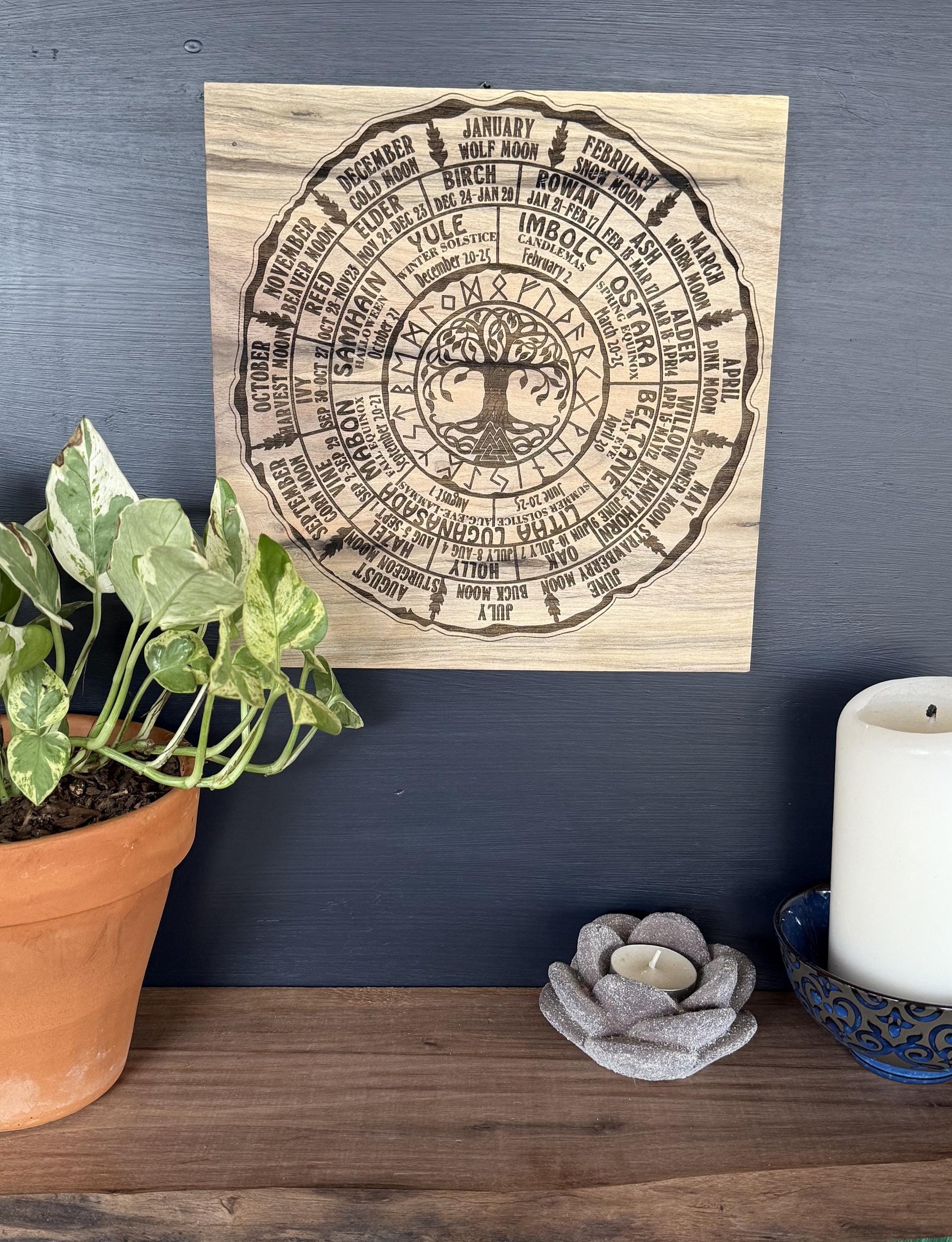 Wooden wall art with Pagan wheel of the year design on a dark blue wall with decorative items below.